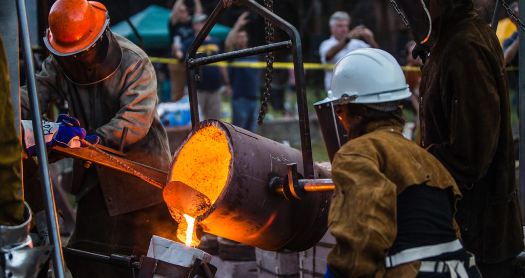 two artists pour ladle of molten iron