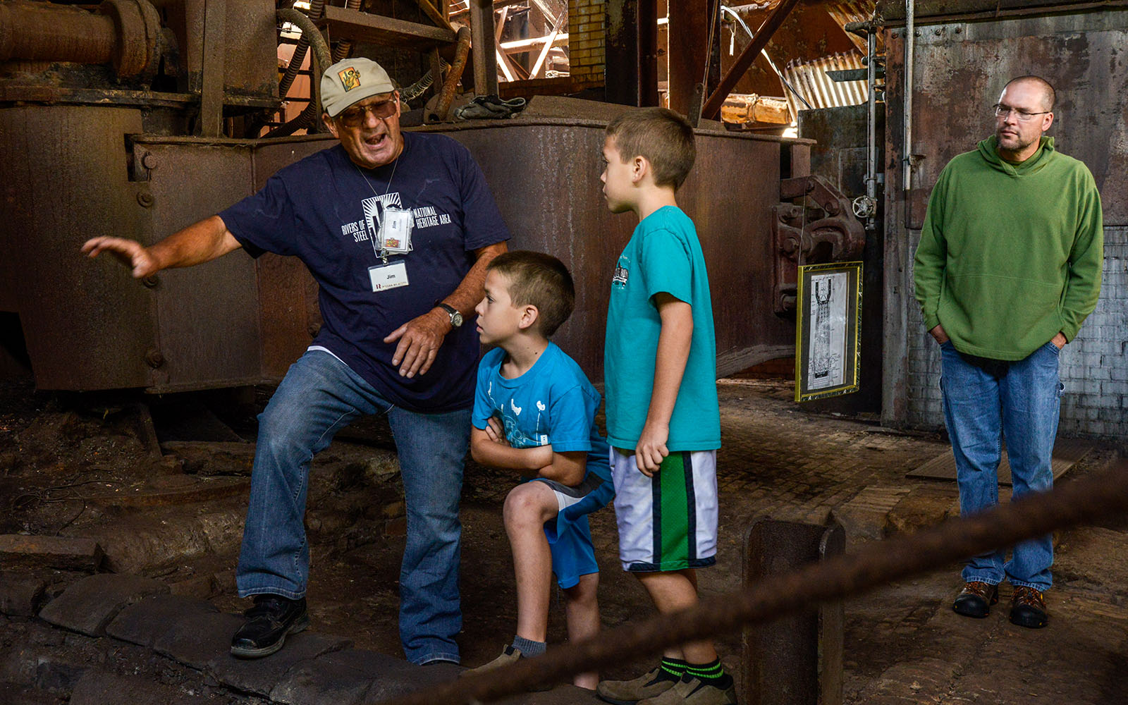 A former steelworker turned tour guide gestures towards furnace #6 with two young boys look attentively with dad in the background.