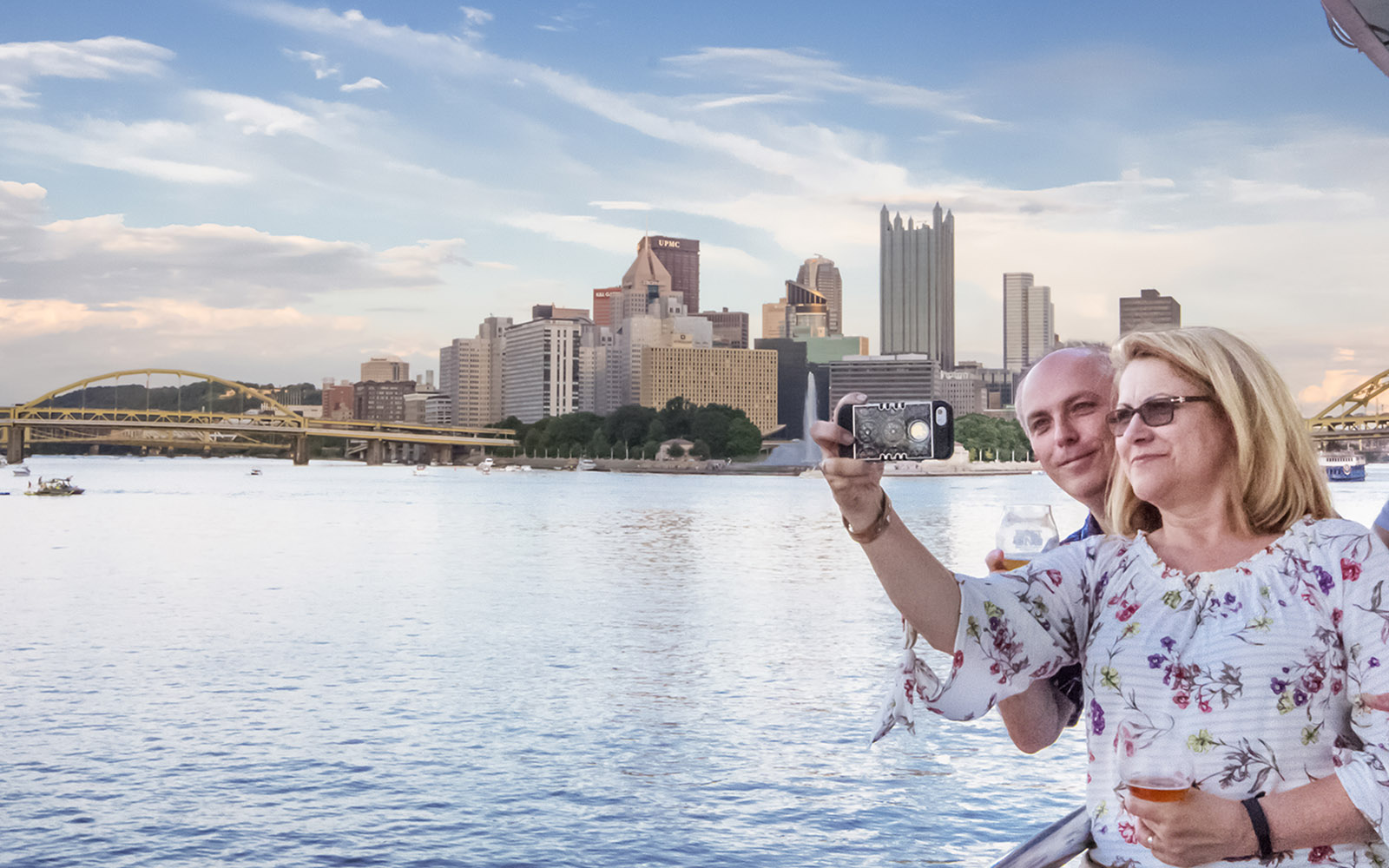 Couple takes a selfie from the riverboat with the skyline of Pittsburgh in the background.