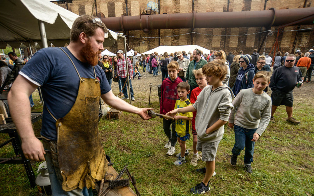 blacksmith shows his hammer to a group of boys