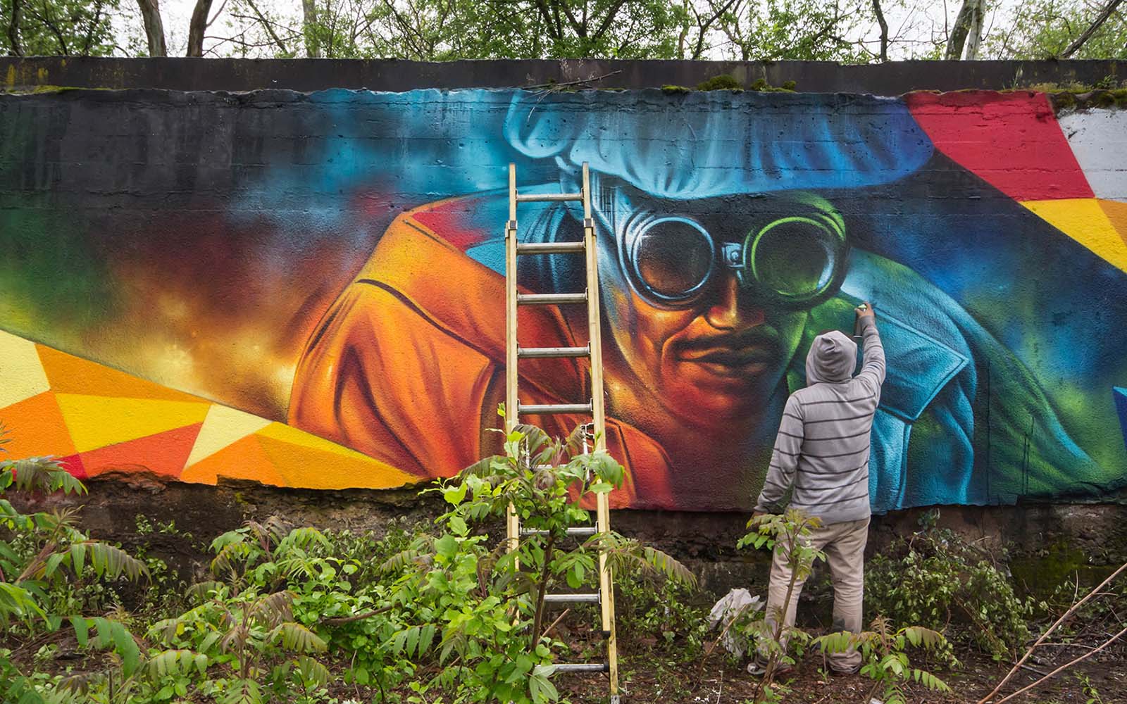 An aerosol artist works on a mural of a steelworker.