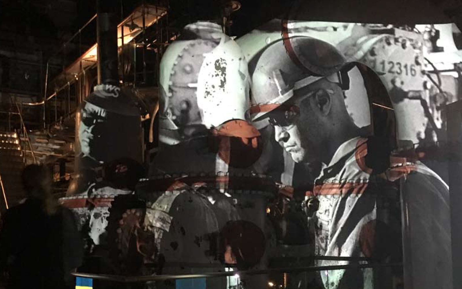 Projection of a man in a hard hat onto an industrial background.