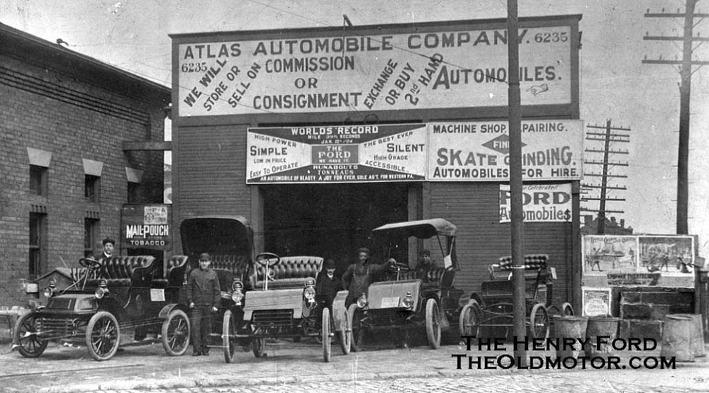Five model T cars and attendants in front of a garage