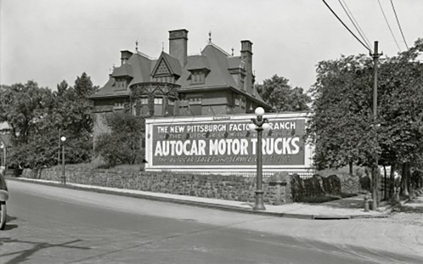 Billboard for "Autocar Motor Trucks" in front of a large victorian mansion.