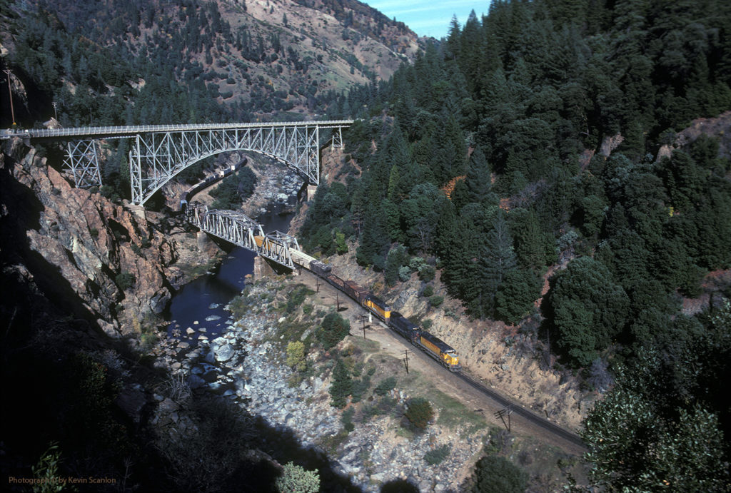 A deep canyon with a steel truss train bridge crossing close to the canyon floor, and a high steel arch bridge passes above it.