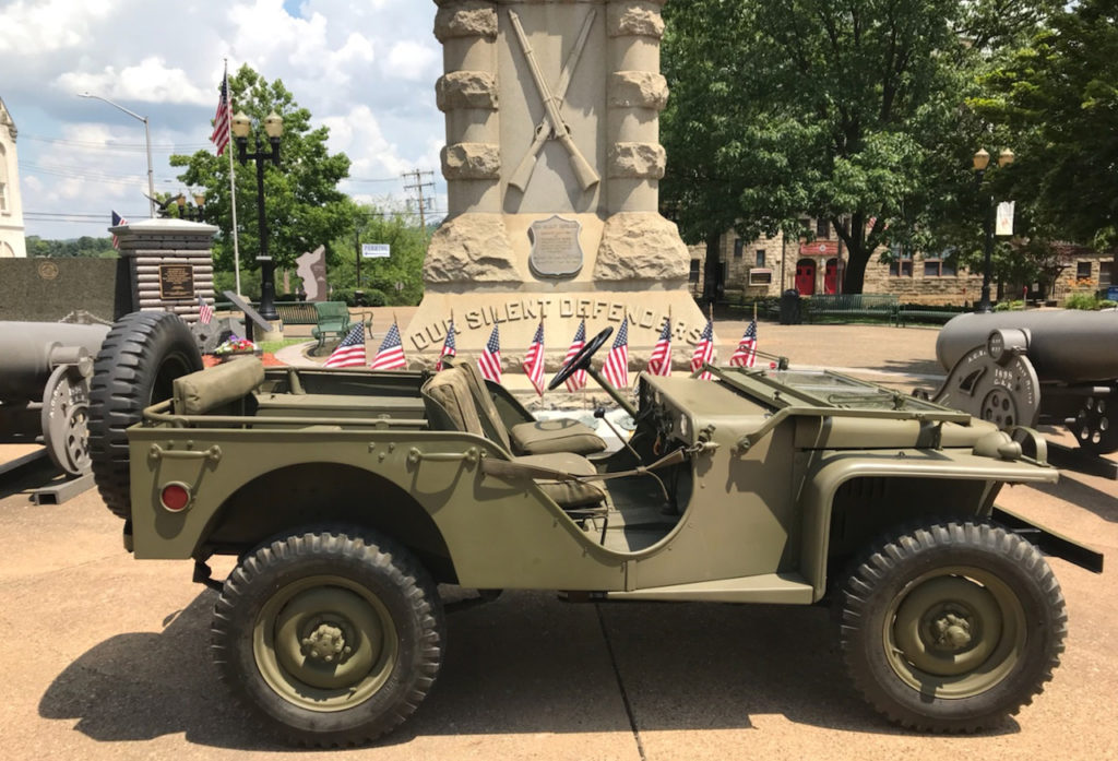 Military Style Jeep with american flags in front of a monument
