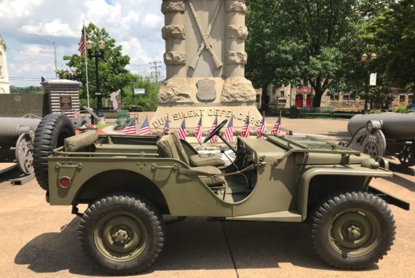 Military Style Jeep with american flags in front of a monument