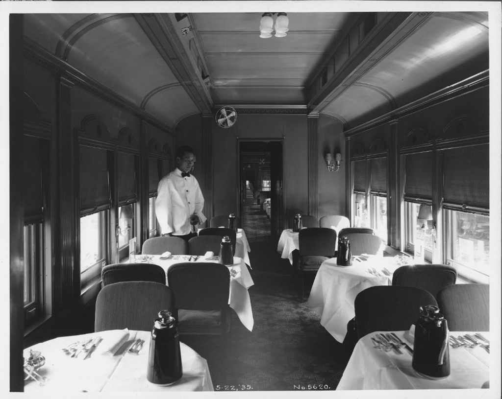 A single porter stand in a unpopulated dining car with dressed table settings.