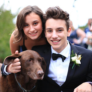 A young woman and man, both in formal dress, pose with their dog.