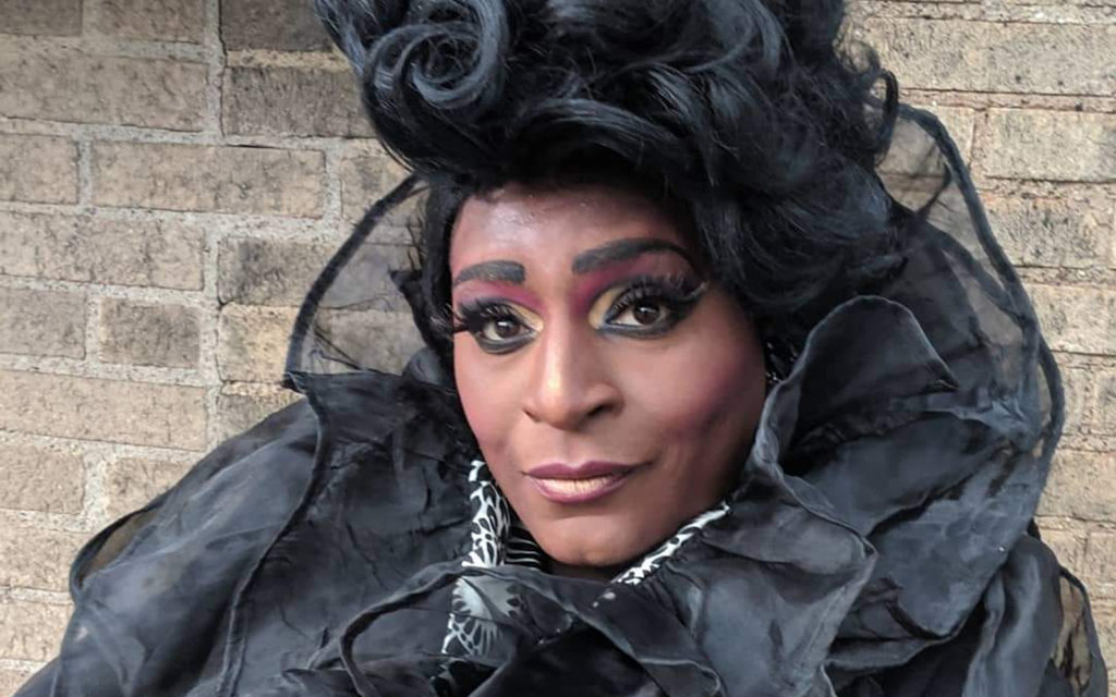 A Black drag queen in black ruffles and styled wig.