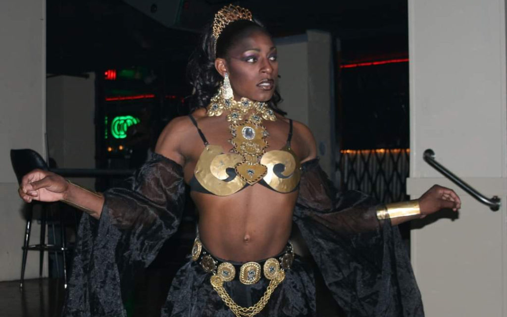 A Black drag queen with a bare midriff decending stairs with arms open.