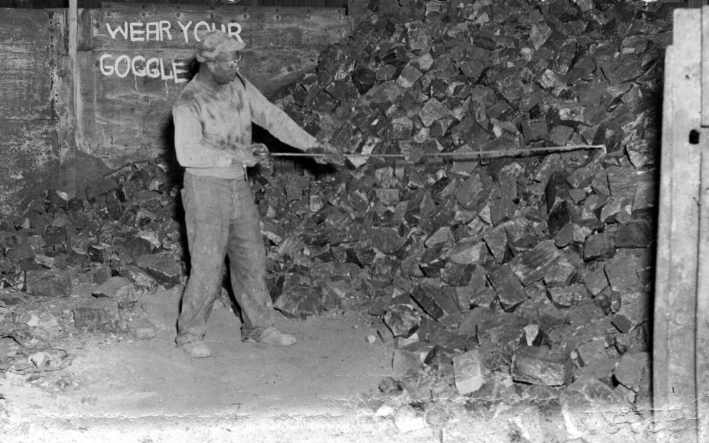 A Black man rakes down manganese from a pile.
