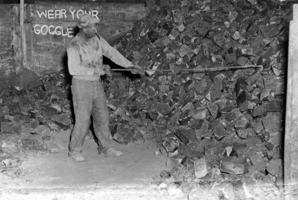 A Black man rakes down manganese from a pile.