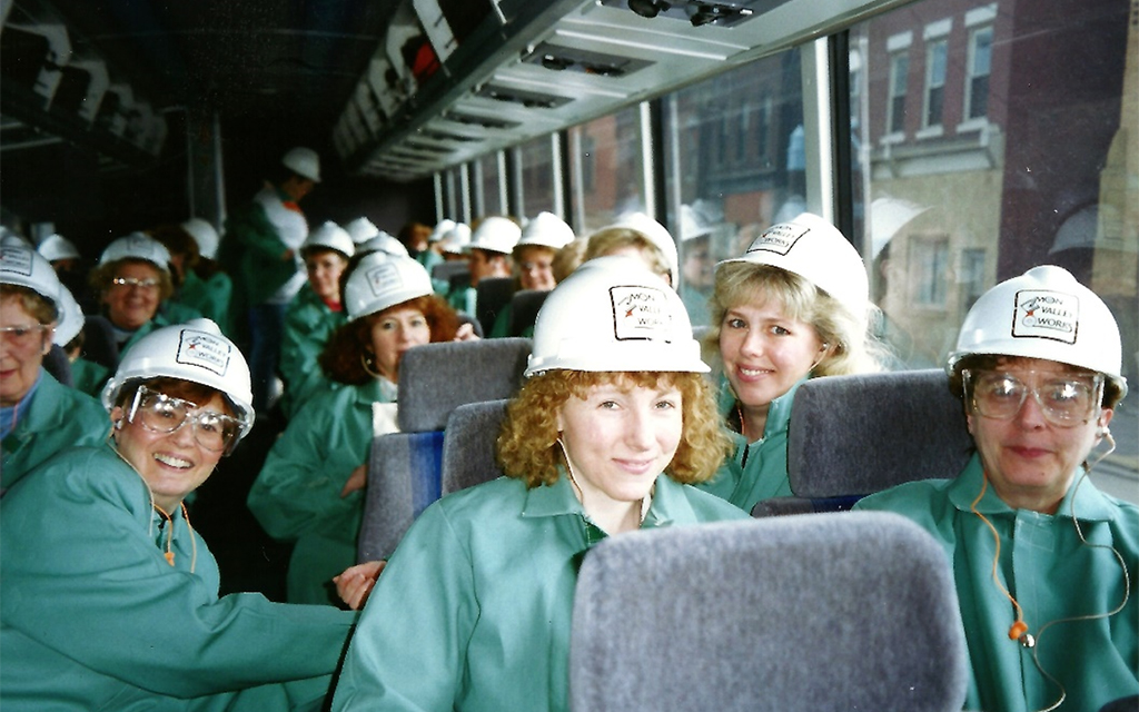 A bus full of women in white hard hats and greens.