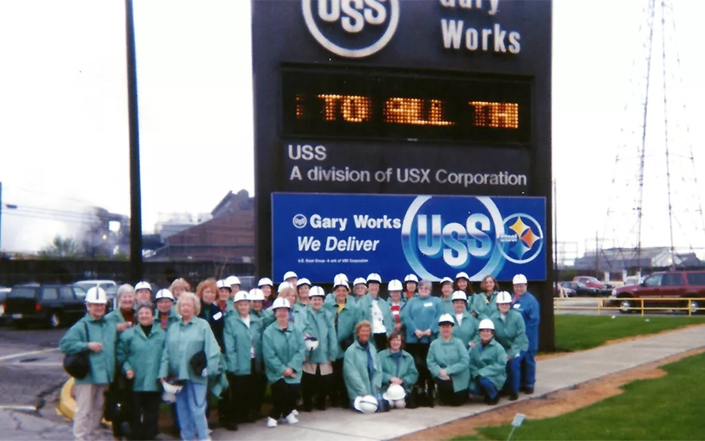 A group of women in greens and white hard hats in front of the Gary Works sign.