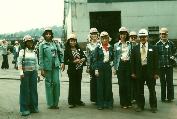 Black and white professional women in hard hats pose outside a mill