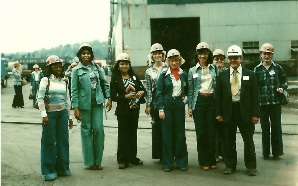 Black and white professional women in hard hats pose outside a mill