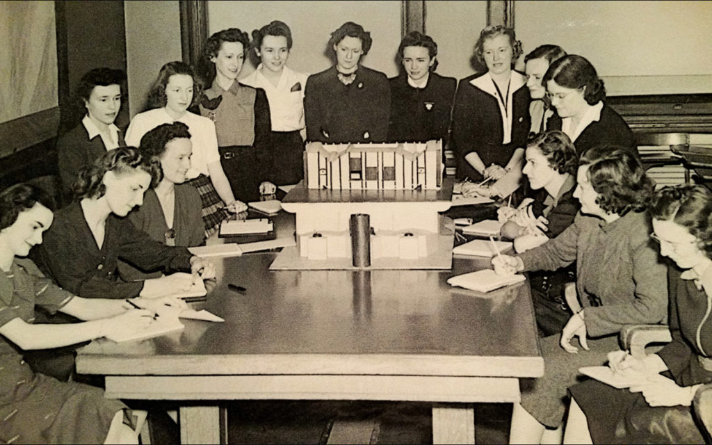 A 1942 photo of 15 professional women gathered around a table.