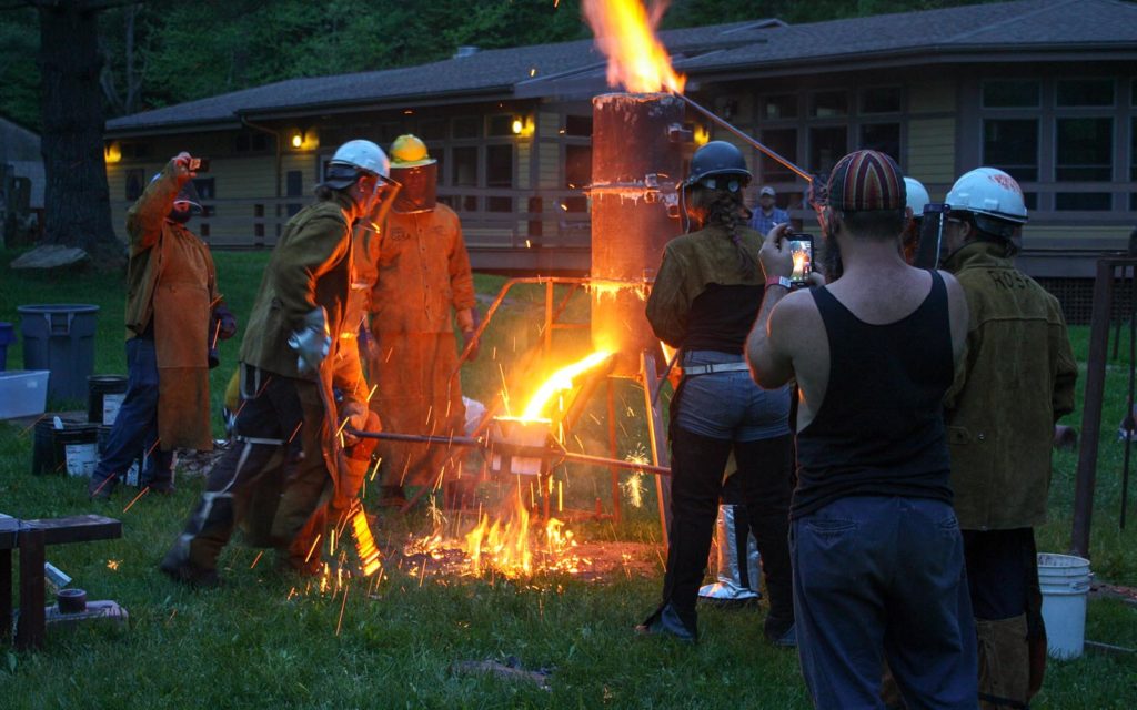 A metal arts crew at dusk work a furnace.