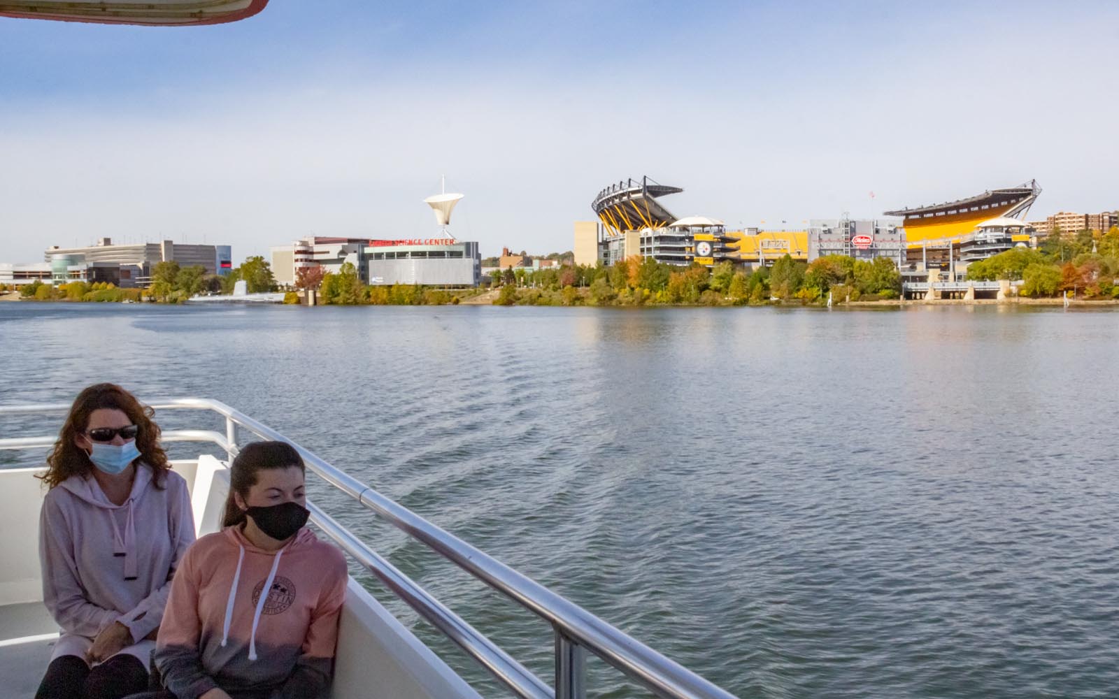 A mother and daughter in masks sit on the boat with the football stadium in the background.
