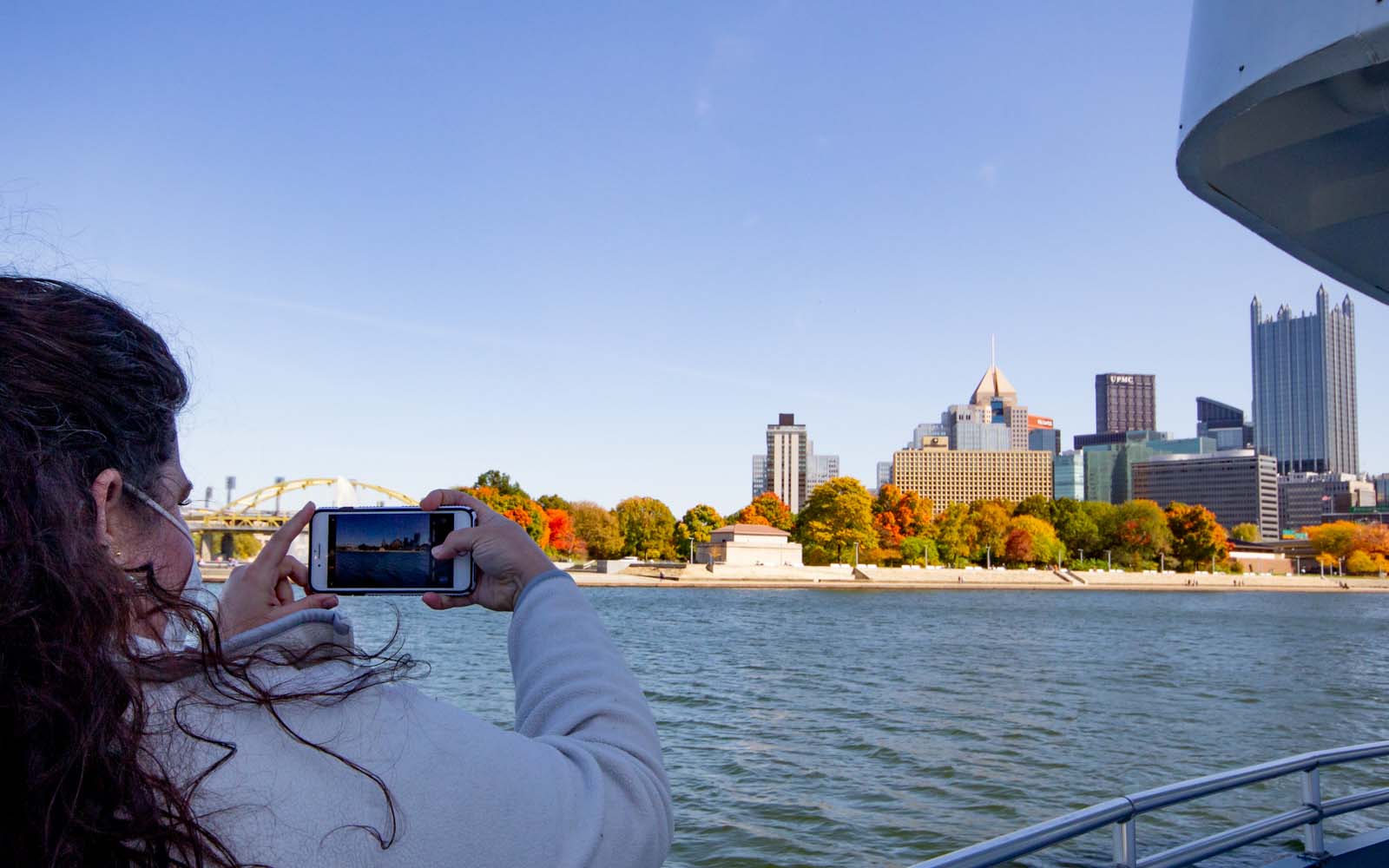 A woman holds her phone up to photograph the downtown skyline from the boat.