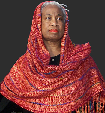 A lux orange shawl with purple details adorns an older black woman.
