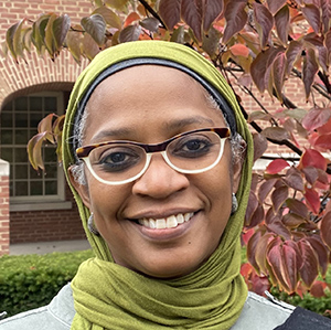 A younger, medium toned black woman with two tone glasses and a pea green headscarf. 