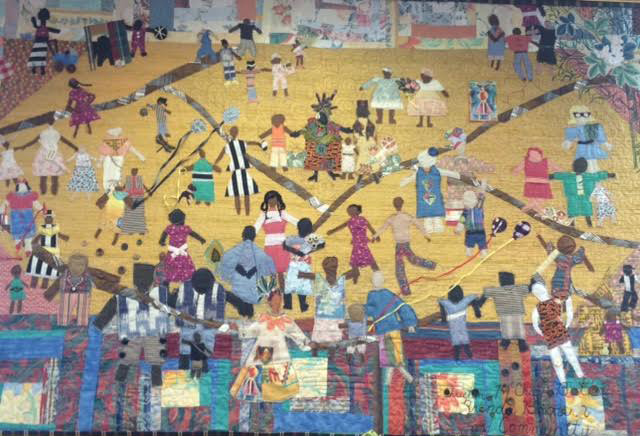 a quilt depicting a street scene with lots of people, mostly Black, and engaged in lots of activities.