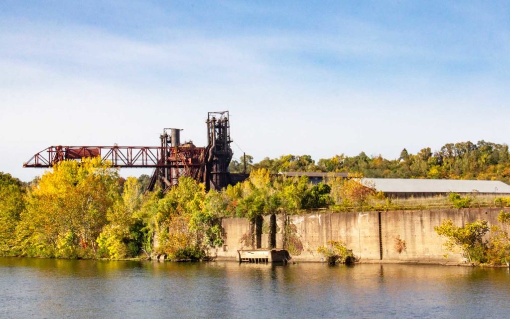 Former iron furnaces and associated buildings see behind a tree lined riverbank.