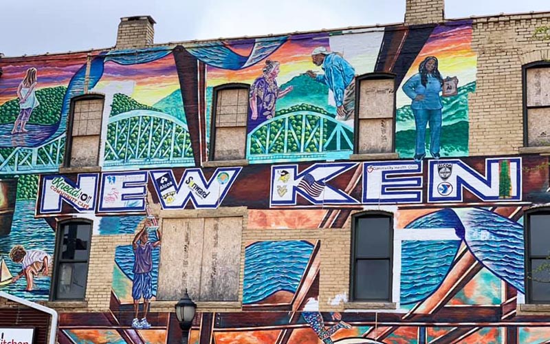 A spray painted mural that reads "New Ken" and depicts aluminum, the bridge, people, etc.