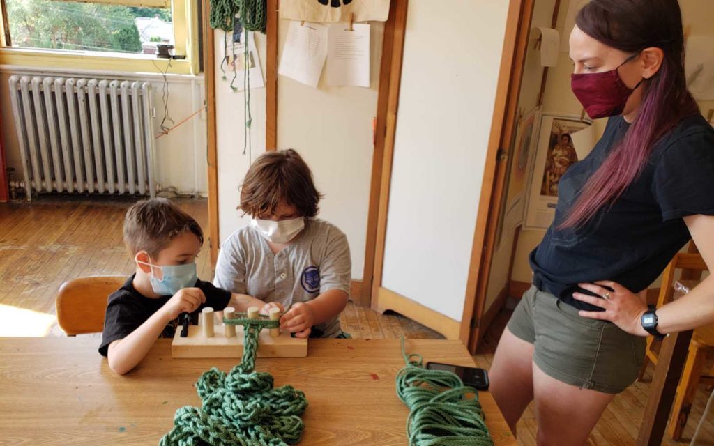Two youth create a large knit yard from a spool.