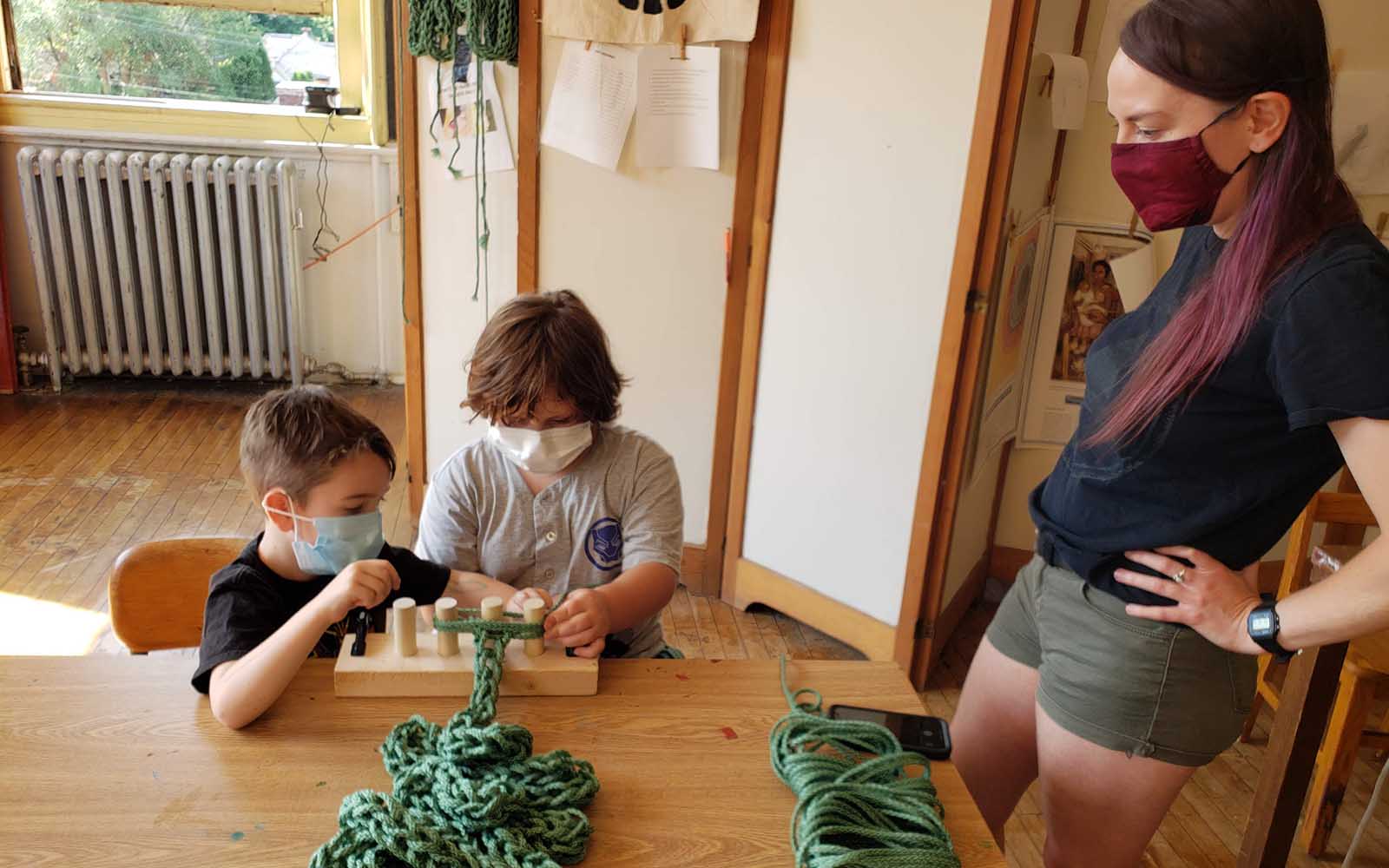 Two youth create a large knit yard from a spool.