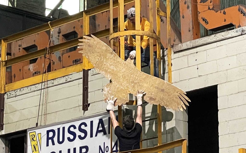 A brass bird is hoisted to a metal cage for support.