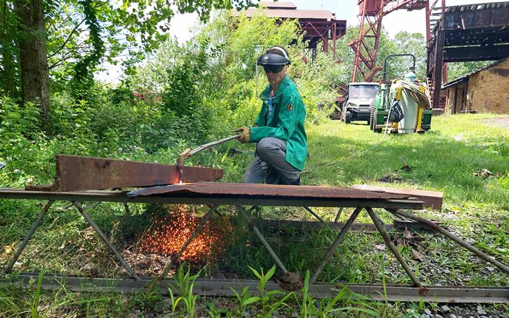 A woman uses a plasma cutter to release sheets of metal from part of a metal structure.