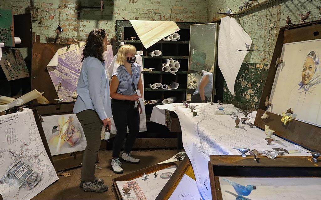 Two visitors look around a room full of drawings and bird figurines. 