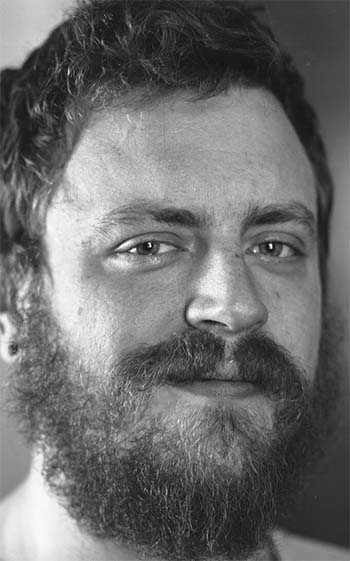 A black and white image of a bearded white man in his late 20s or 30s.
