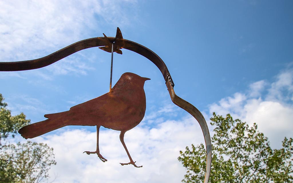 A metal bird sculpture silhouetted by a cloudy blue sky. 