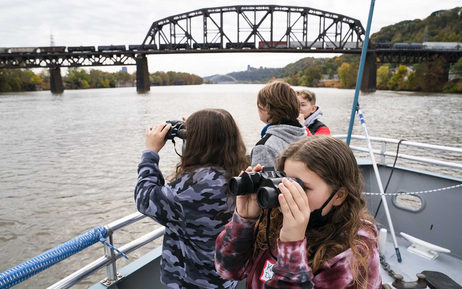 Students look through binoculars on the bow of the Explorer riverboat.
