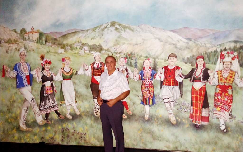 Ed Markoff stands in front of a mural of dancers in the countryside.