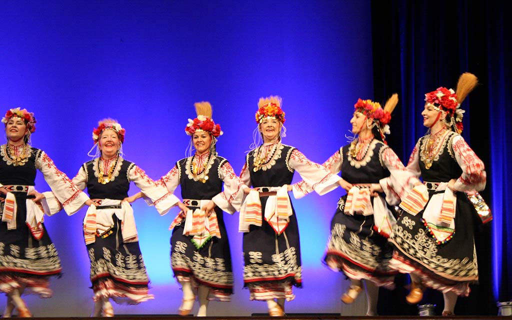 Women in traditional costumes dance together with the arms crossed in front of them.