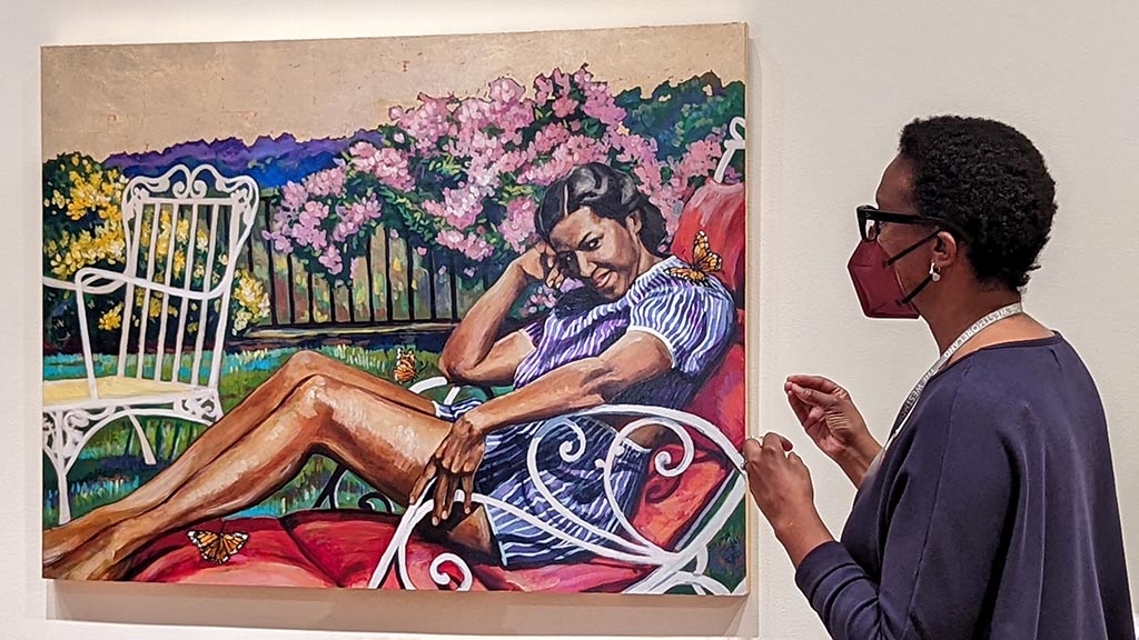 A black woman looks at acolorful painting of a black woman.