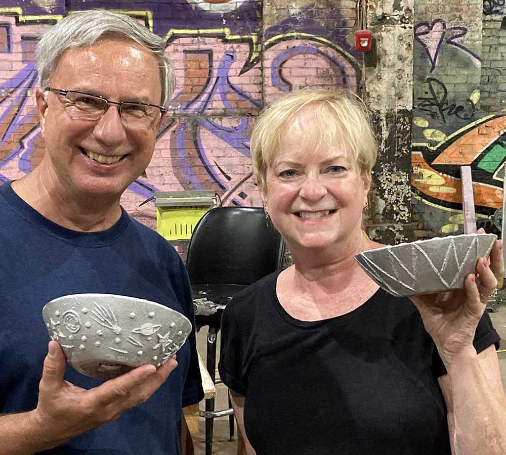 couple holding up carved and cast aluminum bowls