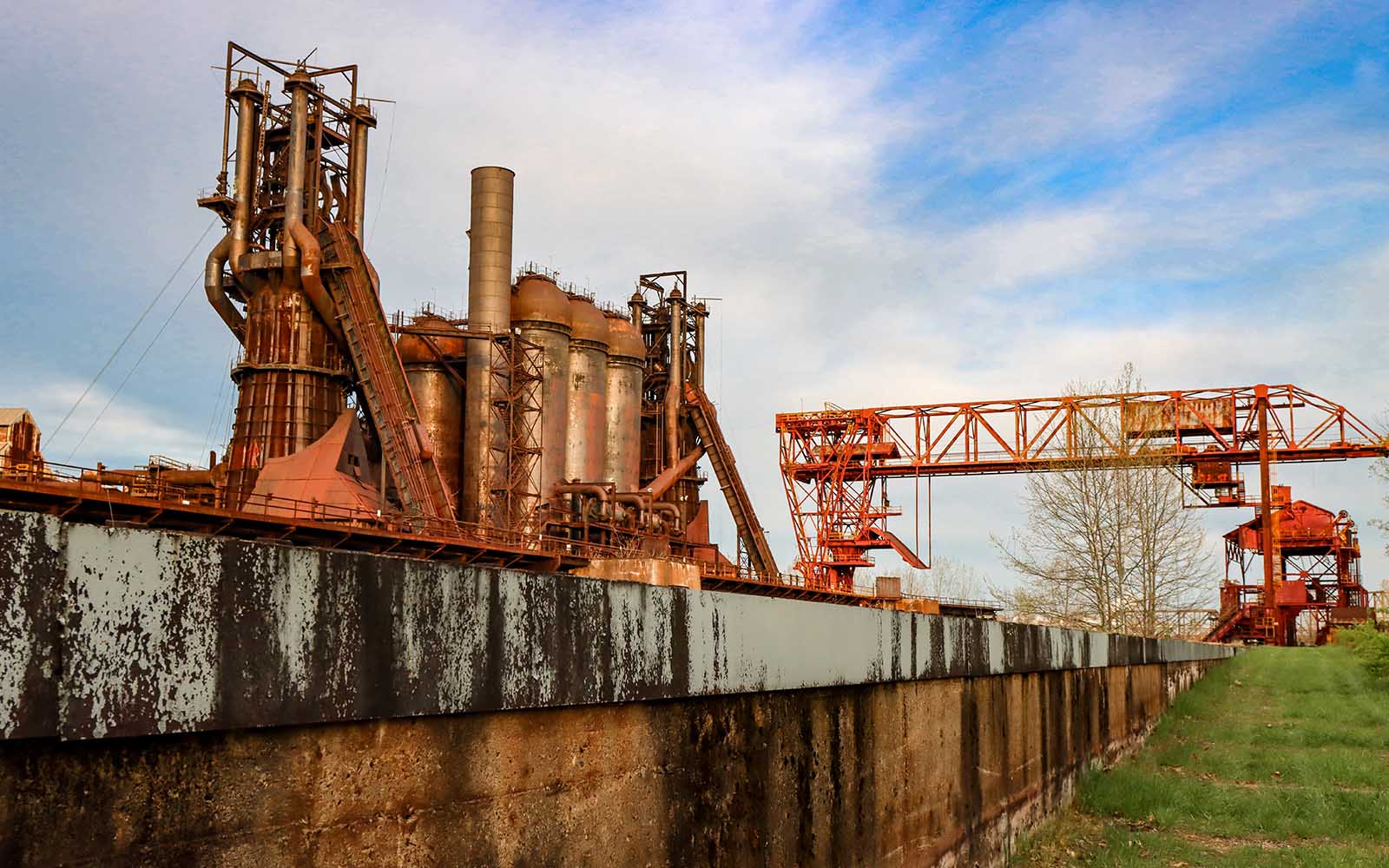 A landscape image of the Carrie Furnaces at sunset with a gritty wall in the foreground.