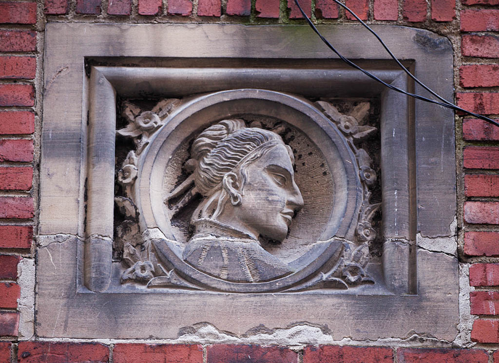 A concrete relief sculpture of a woman's progfile set into a brick wall.