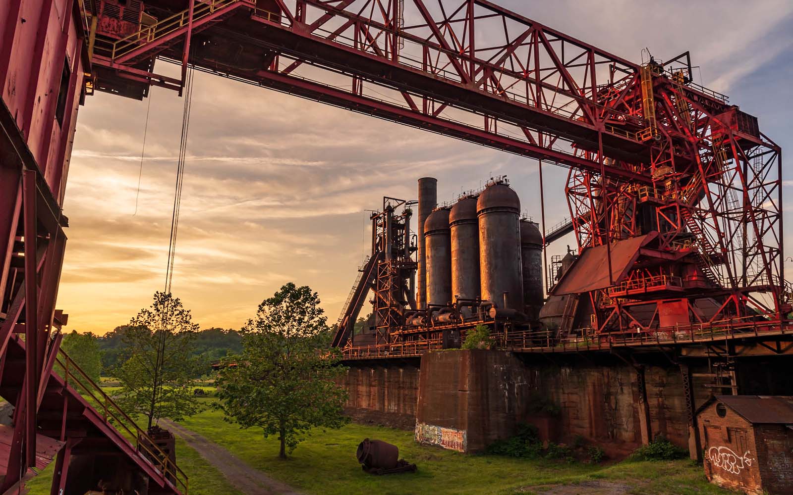 A yellow sunset softly illuminates the stack and stoves of the Carrie Furnaces with an Ore Bridge spanning the foreground of the image.