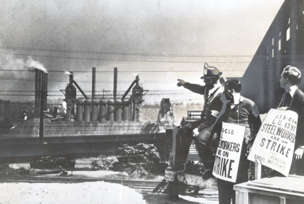 A black and white image of three strikers pointing across the river at blast furnaces.