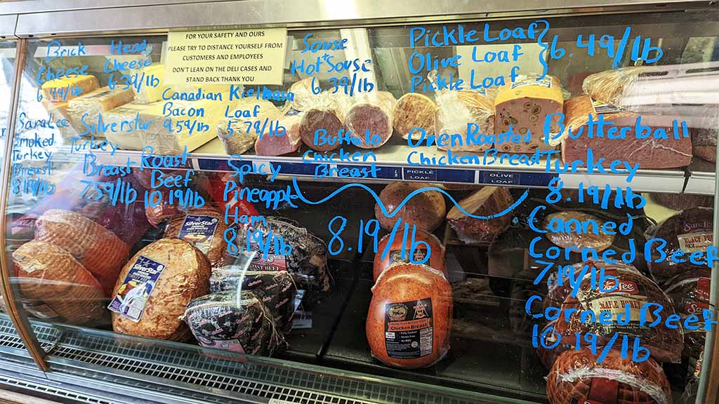 Ham, beef, cheese, and turkey are among the products displayed in this case. Prices are hand-written in blue on the outside of the case.