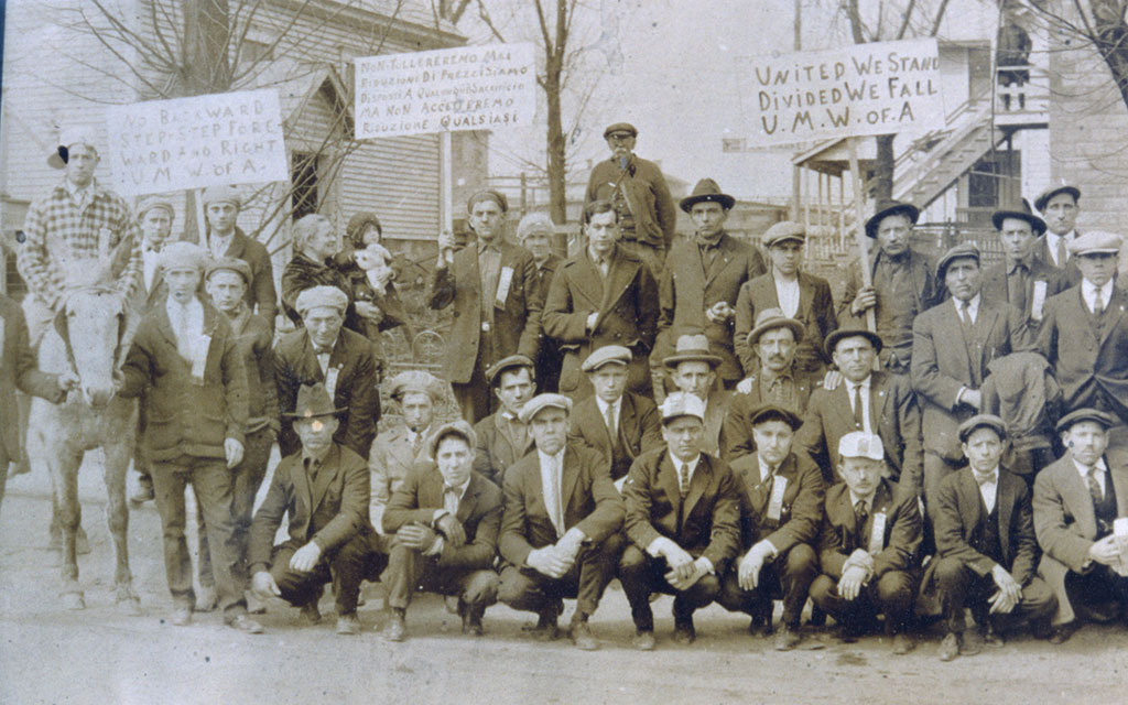 Workers post with picket signs for a group photo. Most are wearing newsboy caps or fedoras.