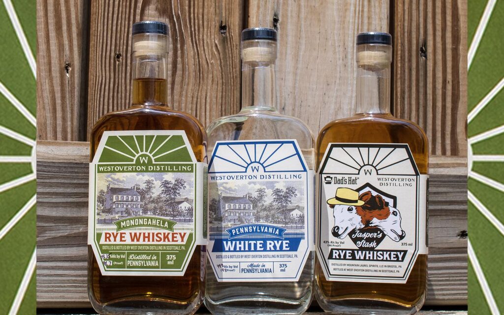 Three liquor bottles: Monongahela Rye, Pennsylvania White Rye, and a Rye Whiskey cobranded with Dad's Hat. 