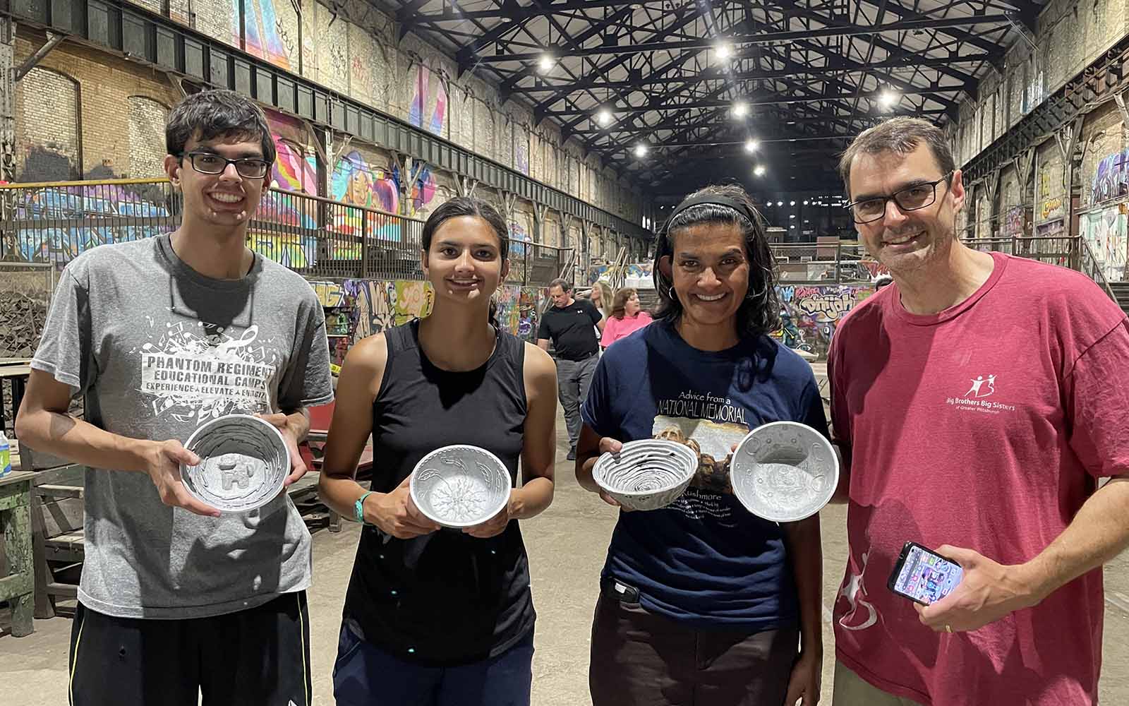 A multicultural group shows off their aluminum doodle bowls.
